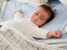 Baby smiling in bed with eyes closed and arms out.